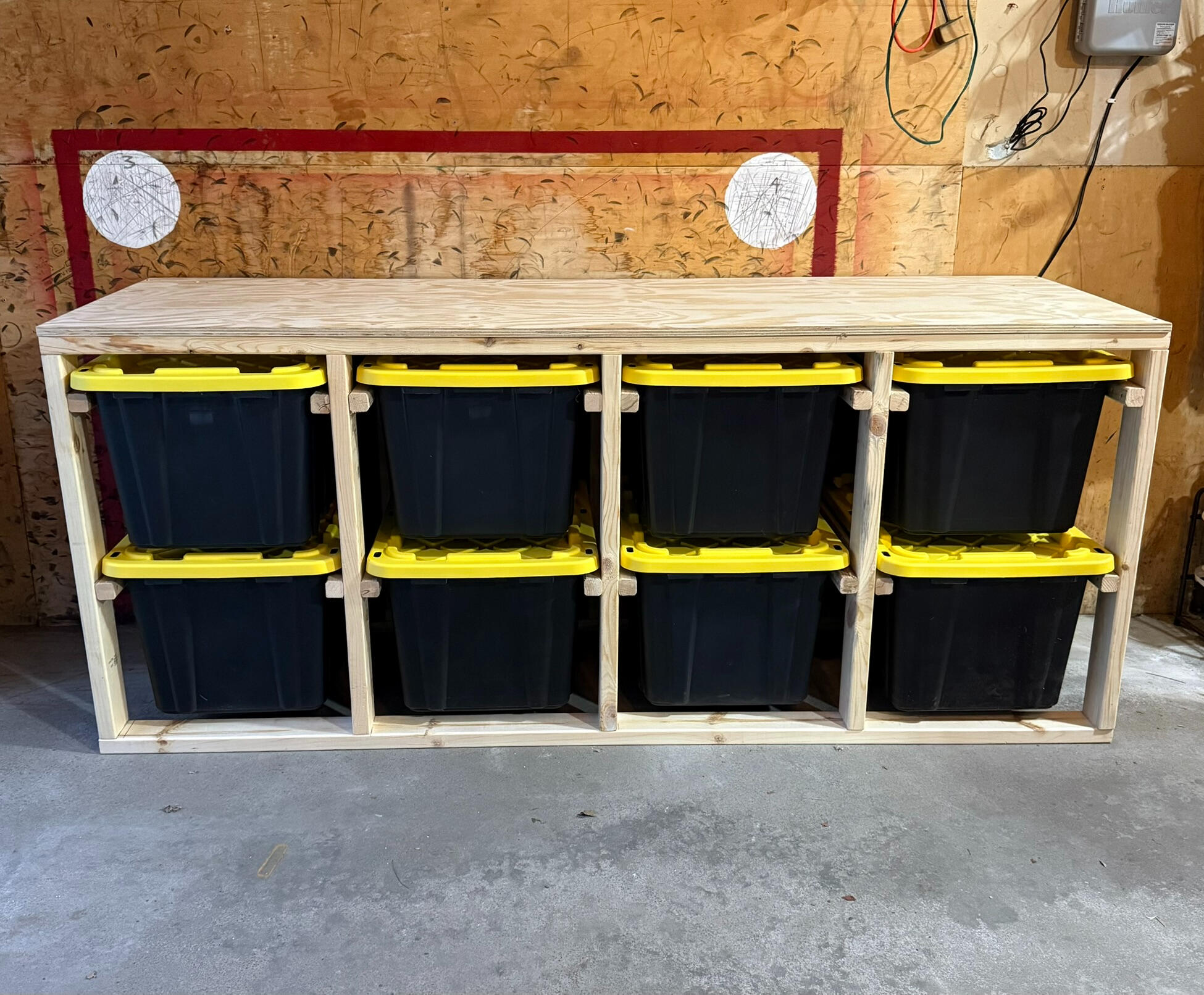 3 wide x 4 high system A cleanly organized garage featuring one wooden bin storage unit that is holding 9 black and yellow storage bins. The unit is 3 wide x 3 high and sits on top of casters.